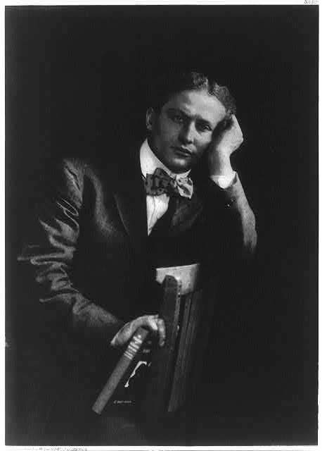 Old black and white photograph of Harry Houdini sitting on a chair, with his hand against his cheek.